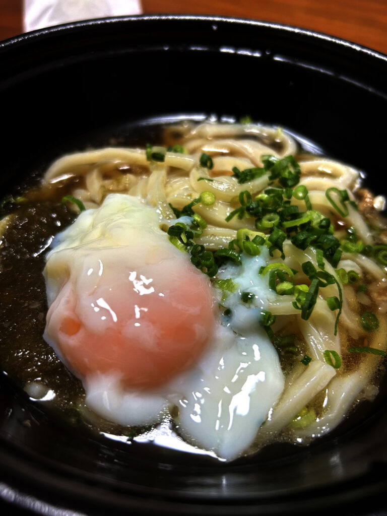 とろとろの半熟温泉卵が絡むかすうどんのアップ